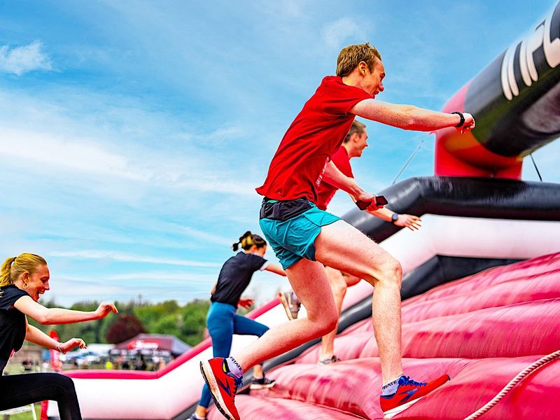 some people in gym clothes running up a large, red inflatable bridge